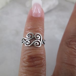 May include: Silver ring with a swirling design, resembling clouds or waves. The ring is worn on a finger.