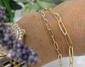 May include: Three gold chain bracelets with different link styles. The bracelets are layered on a person's wrist.