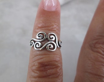 May include: Silver ring with a swirling design, resembling clouds or waves. The ring is worn on a finger.