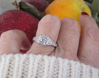 May include: A silver ring with a large, clear, round gemstone surrounded by smaller gemstones. The ring is on a person's finger.