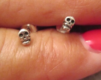 May include: A pair of silver skull stud earrings. The earrings are small and delicate, and they are perfect for adding a touch of edgy style to any outfit.