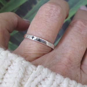 May include: A silver ring with a small cross design. The ring is worn on a finger.