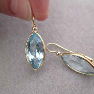 May include: A pair of gold earrings with light blue marquise-shaped gemstones.
