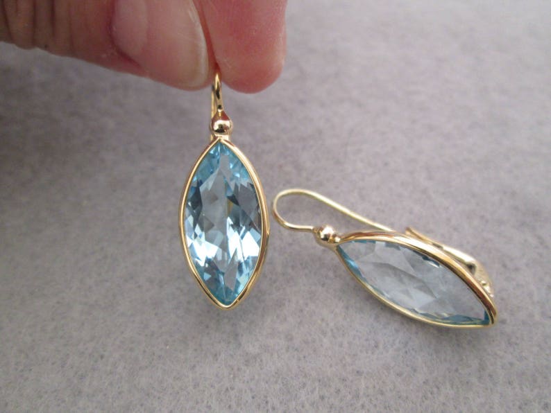 May include: A pair of gold earrings with light blue marquise-shaped gemstones.