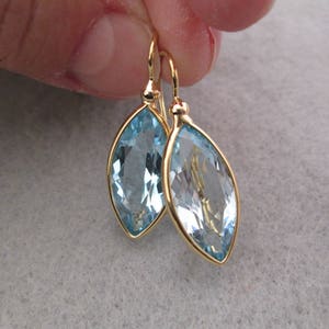 May include: A pair of gold earrings with light blue marquise-shaped gemstones.