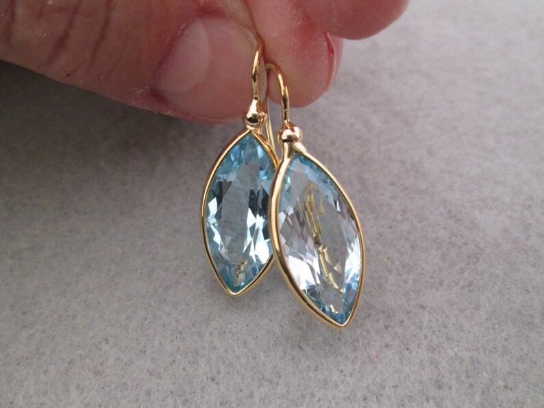 May include: A pair of gold earrings with light blue marquise-shaped gemstones.