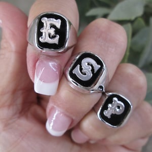 May include: Three silver rings with black enamel and white letters. The rings feature the letters E, S, and P.