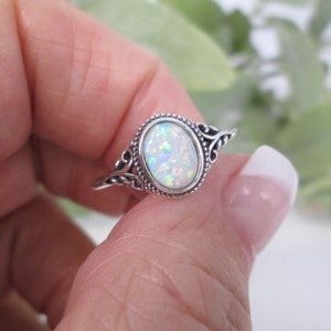 May include: A silver ring with an oval-shaped opal gemstone. The ring has a delicate, ornate design.