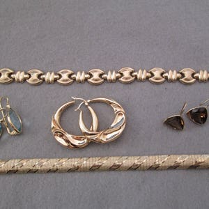 May include: A set of gold jewelry including a chain bracelet, two pairs of earrings, and a gold bangle bracelet.
