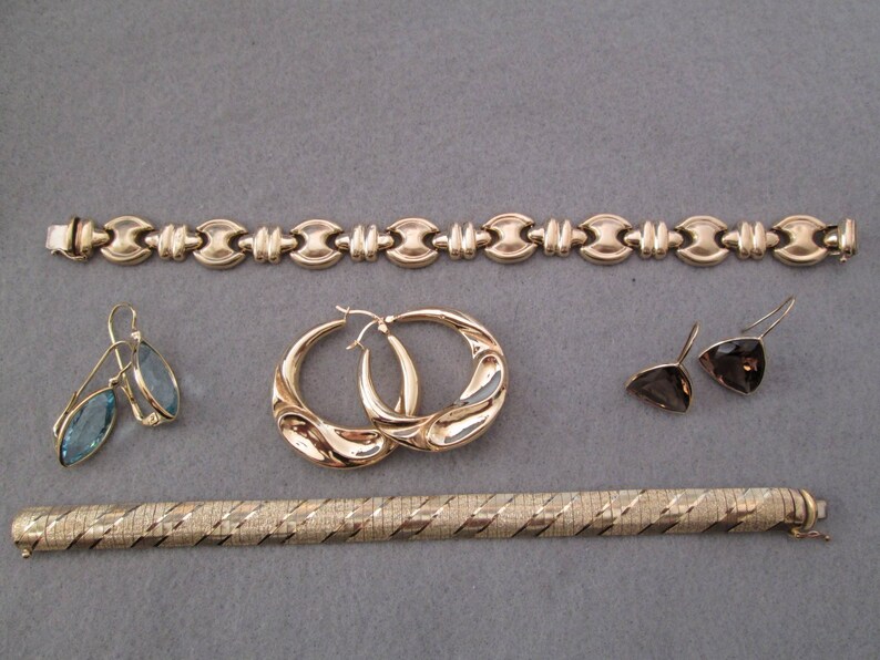 May include: A set of gold jewelry including a chain bracelet, two pairs of earrings, and a gold bangle bracelet.