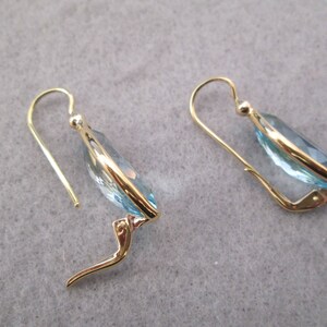 May include: A pair of gold earrings with light blue teardrop-shaped stones.