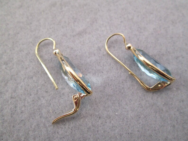 May include: A pair of gold earrings with light blue teardrop-shaped stones.