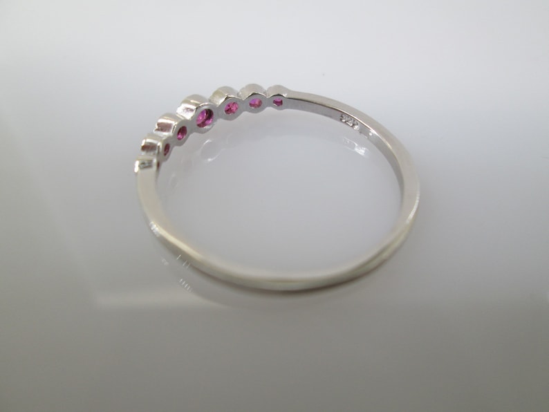 Pu&ograve; includere: Un anello a fascia d'argento con una fila di pietre preziose rosa incastonate nella fascia.