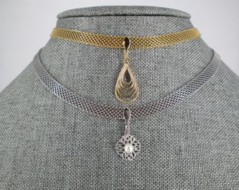 May include: Two necklaces displayed on a gray mannequin head. The top necklace is gold-toned with a teardrop pendant. The bottom necklace is silver-toned with a floral pendant and a pearl center. Both necklaces have a mesh chain.
