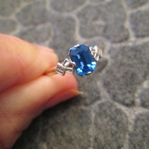 May include: A silver ring with a blue gemstone set in a prong setting. The ring has a delicate design with small accents.