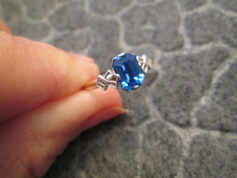 May include: A silver ring with a blue gemstone set in a prong setting. The ring has a delicate design with small accents.