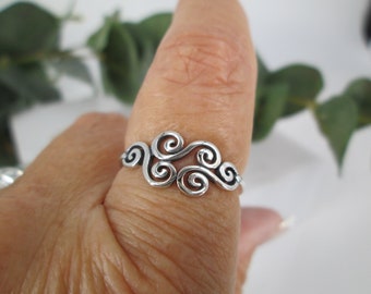 May include: A silver ring with a swirling design. The ring is on a person's finger.