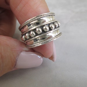 May include: A silver ring with a beaded design. The ring is wide and has a textured band.