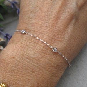 May include: A delicate silver chain bracelet with three small round clear stones.
