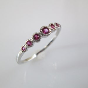 Pu&ograve; includere: Un anello a fascia d'argento con una fila di sei piccole pietre rotonde rosa.