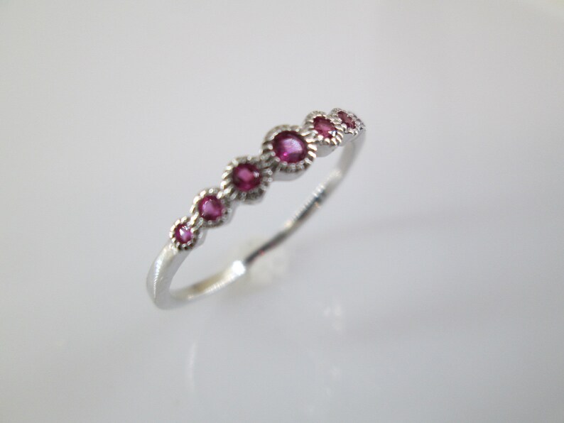 Pu&ograve; includere: Un anello a fascia d'argento con una fila di sei piccole pietre rotonde rosa.