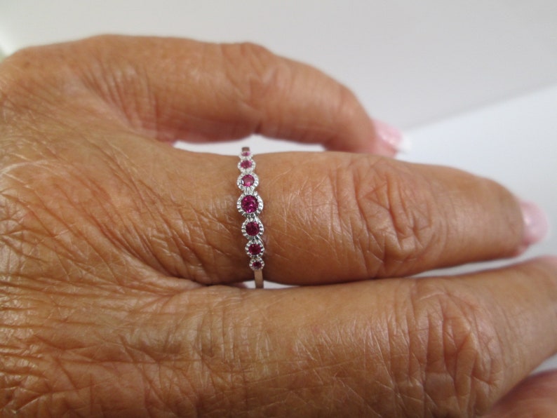 Pu&ograve; includere: Un anello a fascia d'argento con una fila di piccole pietre rotonde rosse.
