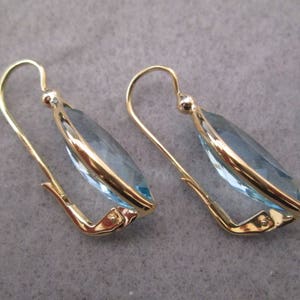 May include: A pair of gold earrings with light blue teardrop-shaped gemstones.