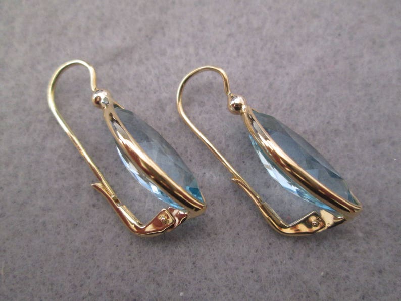 May include: A pair of gold earrings with light blue teardrop-shaped gemstones.