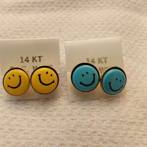 May include: Two pairs of 14KT gold smiley face earrings. One pair is yellow and the other is blue.