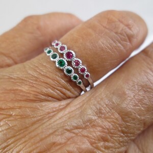Pu&ograve; includere: Due anelli d'argento con piccole pietre preziose verdi e rosse. Gli anelli sono impilati su un dito.