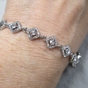 May include: A silver bracelet with a row of square-shaped crystal accents. Each square has a smaller crystal in the center.
