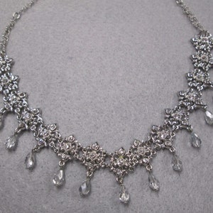 May include: A silver necklace with a delicate chain and a floral design. The necklace features dangling crystal drops.