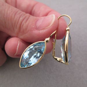 May include: A pair of gold earrings with marquise-shaped blue topaz gemstones. The earrings have a simple, elegant design.