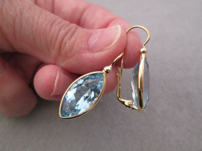 May include: A pair of gold earrings with marquise-shaped blue topaz gemstones. The earrings have a simple, elegant design.