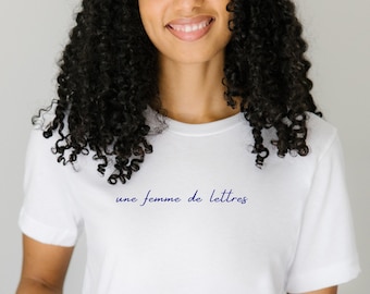 May include: White t-shirt with the text "une femme de lettres" in blue cursive writing.