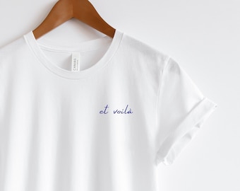 May include: White t-shirt with a blue embroidered phrase "et voilà" on the front.
