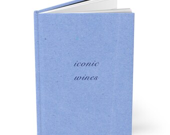 May include: A hardcover book with a light blue, textured cover. The front cover features the text "iconic wines" printed in a dark blue, italicized serif font. The book is slightly open, revealing white pages at the top edge of the binding.