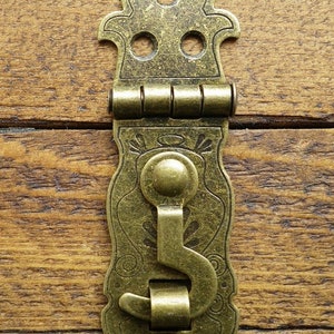 May include: Antique brass latch with a decorative design and a hook. The latch has a hinge and a small knob.