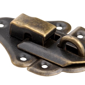 May include: Antique brass latch with a decorative design and a loop handle. The latch is made of metal and has a dark brown finish.