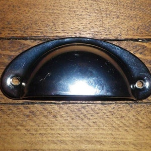 May include: A black metal cup pull handle with a rounded top and two holes on the sides.