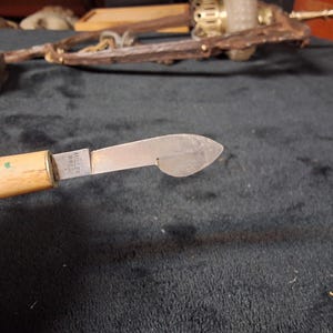 May include: Close-up of a vintage knife with a light-colored wooden handle and a silver blade. The blade has a unique shape and is marked "MILLER BROS. USA". The knife is likely an antique tool.