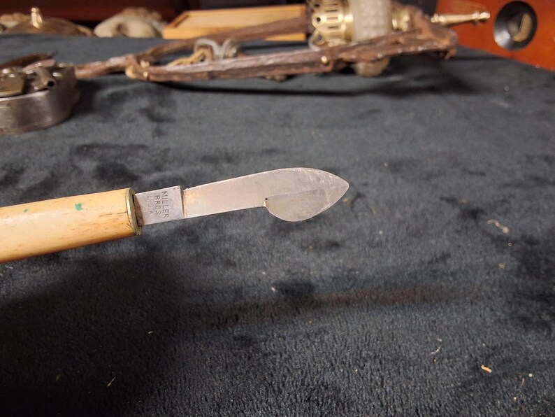 May include: Close-up of a vintage knife with a light-colored wooden handle and a silver blade. The blade has a unique shape and is marked "MILLER BROS. USA". The knife is likely an antique tool.