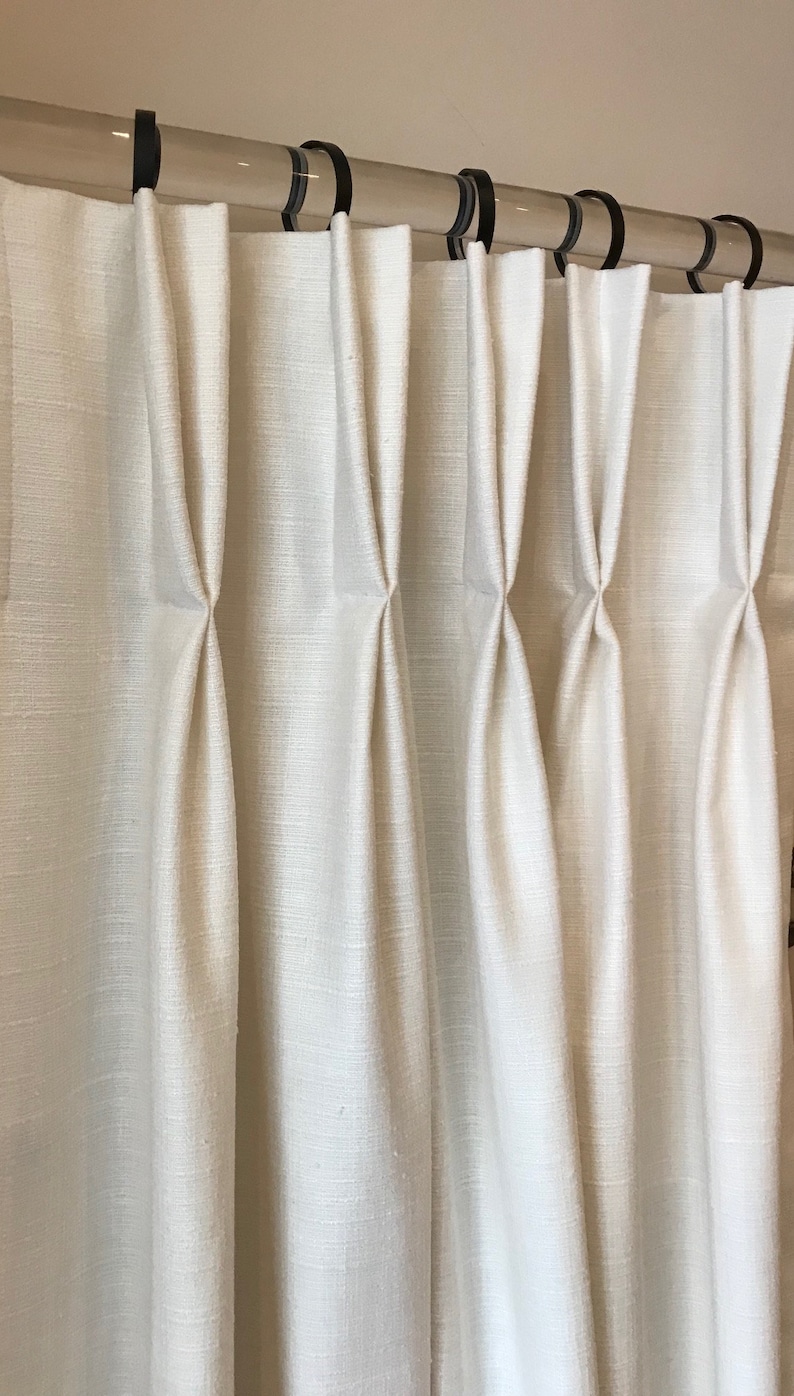 May include: White curtains with pleats hanging from a clear acrylic rod with black rings.
