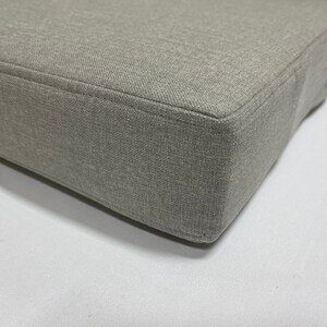 May include: A close-up of a gray fabric cushion with a smooth, even texture. The cushion is rectangular and has a slightly rounded edge.