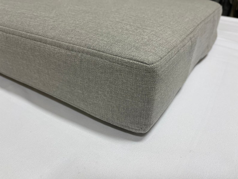 May include: A close-up of a gray fabric cushion with a smooth, even texture. The cushion is rectangular and has a slightly rounded edge.