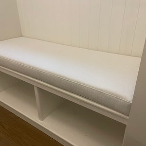 Puede incluir: Banco acolchado blanco con dos estantes abiertos debajo. El banco est&aacute; integrado en una pared con lambr&iacute;n blanco.