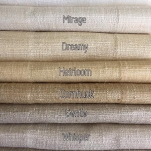 May include: A stack of eight fabric swatches in various shades of beige and white. The swatches are labeled with names like "Pearl", "Mirage", "Dreamy", "Heirloom", "Cornhusk", "Gentle", "Whisper", and "Feather".