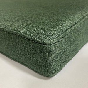 Puede incluir: Primer plano de un coj&iacute;n cuadrado verde oscuro con tejido texturizado. El coj&iacute;n est&aacute; hecho de un material suave y duradero y tiene un brillo sutil.