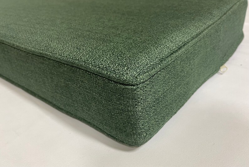 Puede incluir: Primer plano de un coj&iacute;n cuadrado verde oscuro con tejido texturizado. El coj&iacute;n est&aacute; hecho de un material suave y duradero y tiene un brillo sutil.