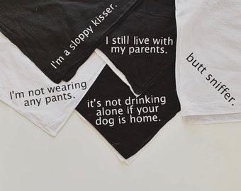 May include: Four black and white fabric bandanas with humorous text printed on them. The text reads: "I'm a sloppy kisser", "I'm not wearing any pants", "I still live with my parents", and "It's not drinking alone if your dog is home".